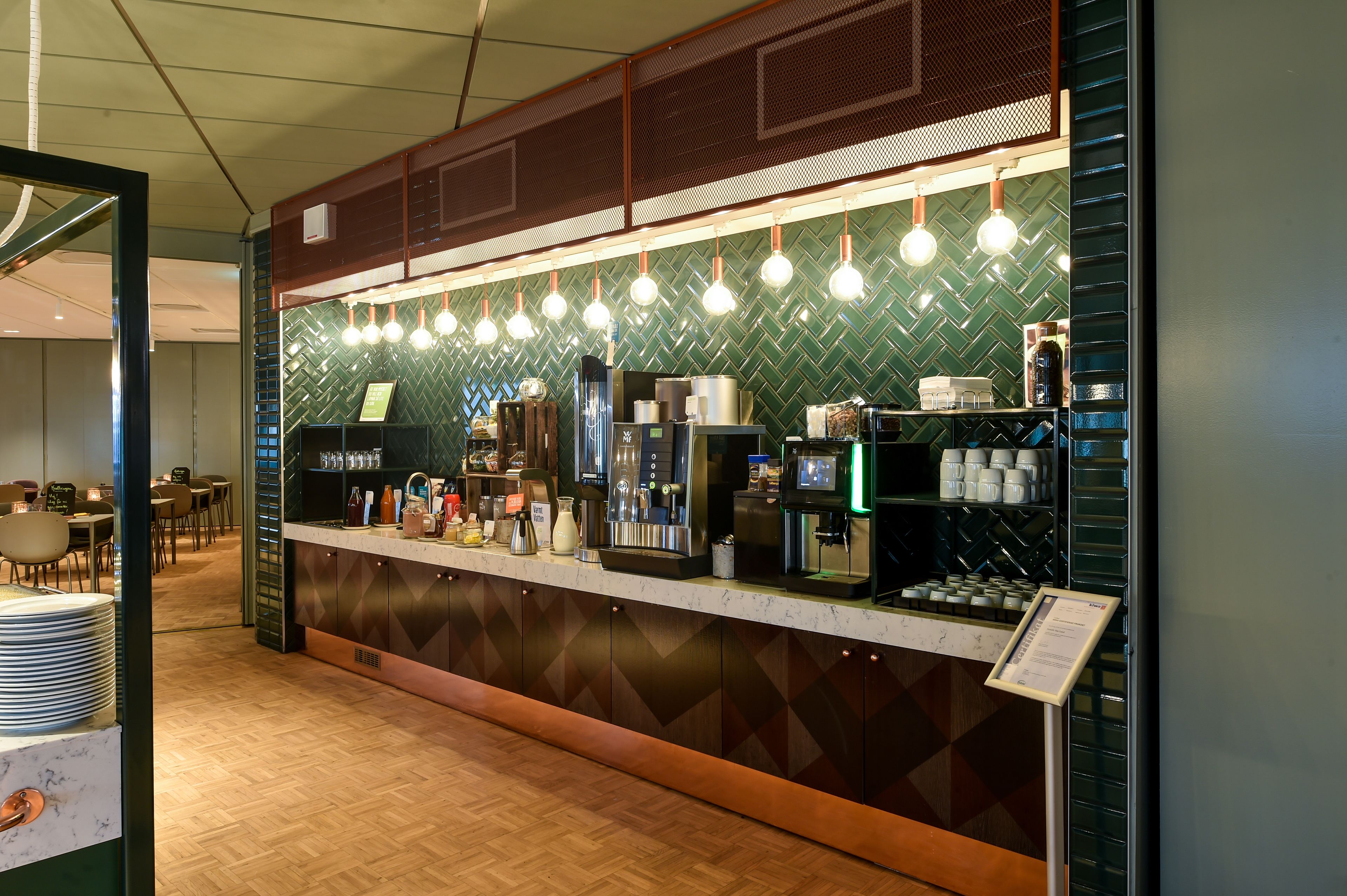 Un área de bar moderna con mostrador, máquinas de café y una pantalla de menú.