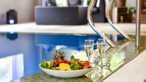 A poolside setting with a bowl of fruit and two glasses of champagne on a reflective surface. - Scandic Star (Lund)