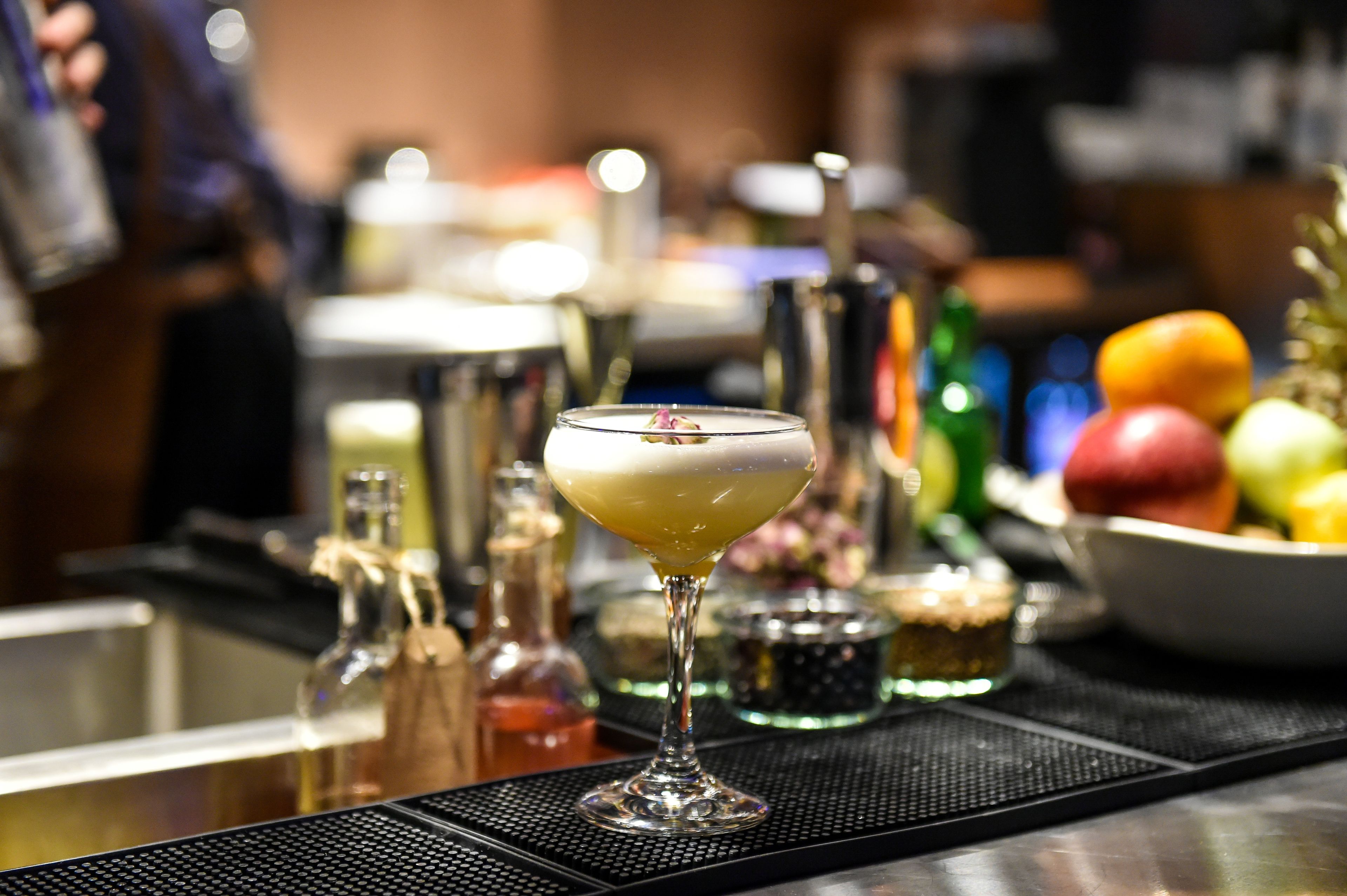 Zona de bar con una copa de cóctel, utensilios de bar y un bol de fruta.