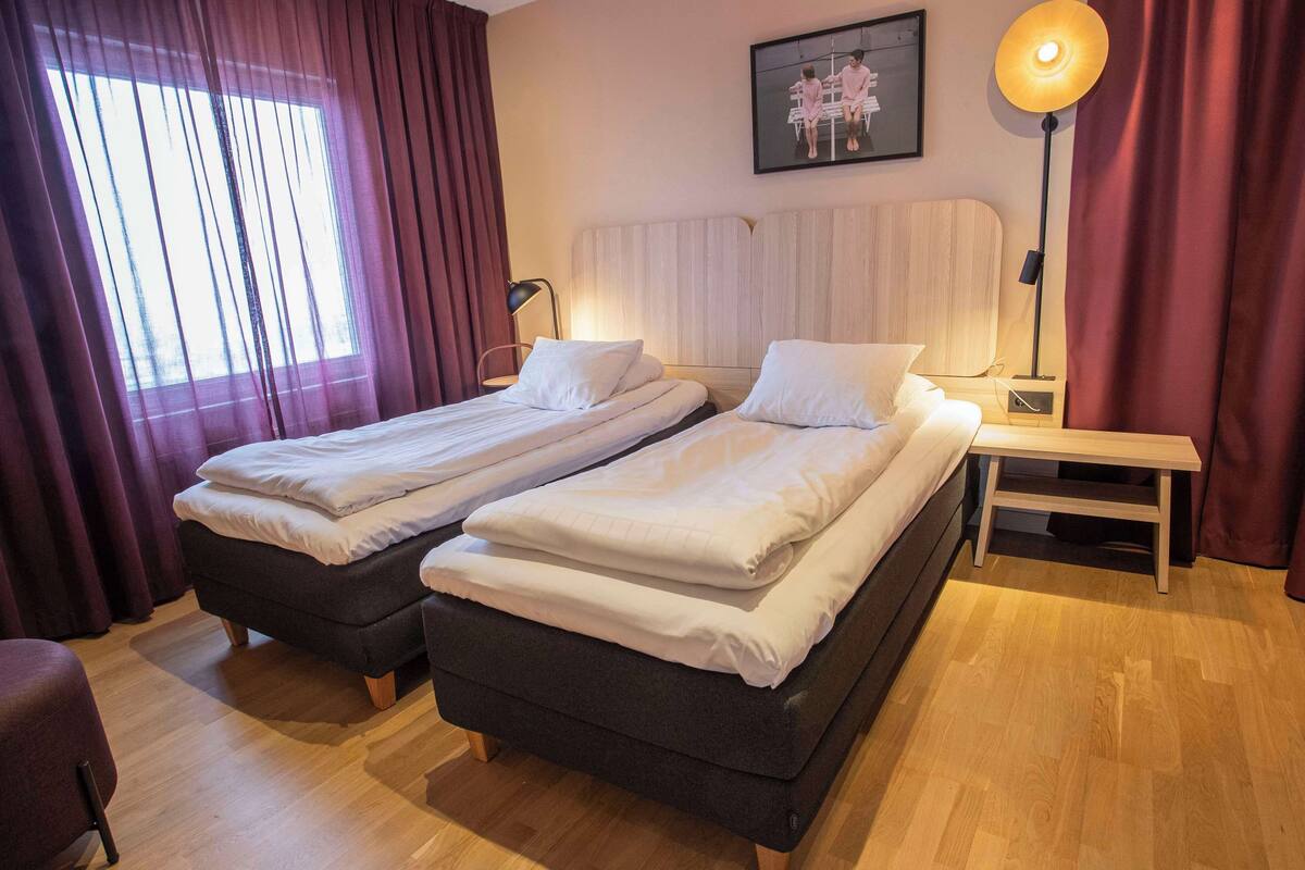 Ein Hotelzimmer mit zwei Betten, einem Nachttisch, einer Lampe und einem Gemälde an der Wand.