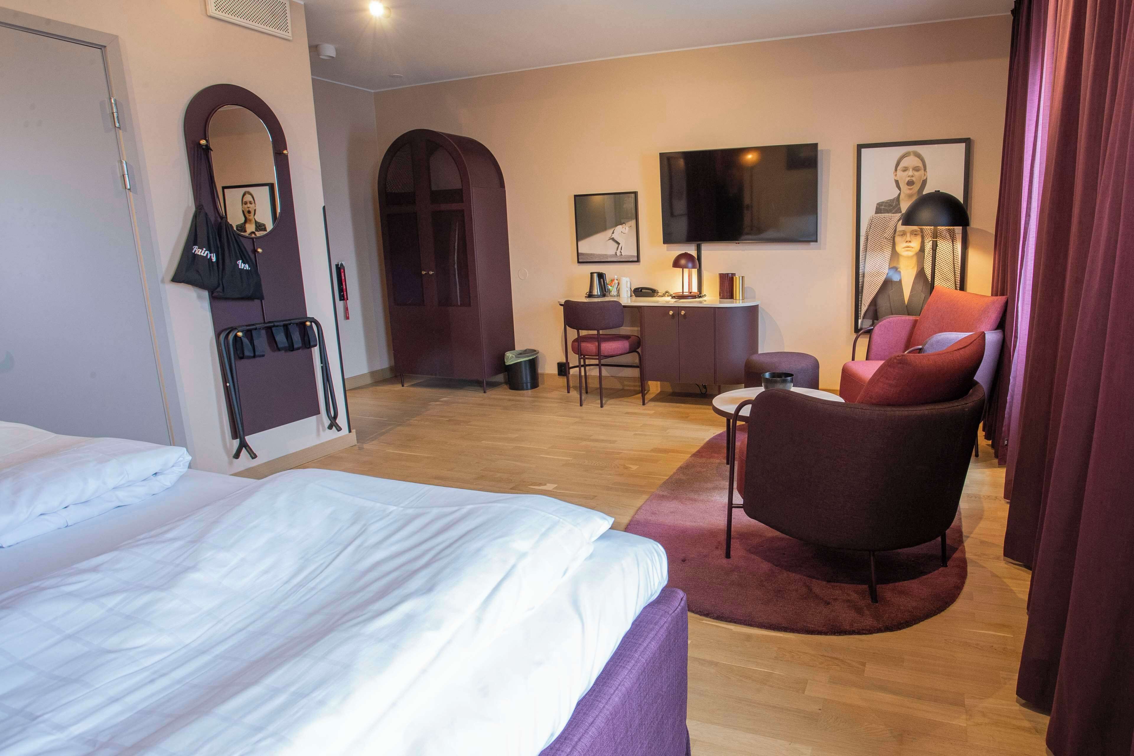 Habitación de hotel con cama, escritorio, silla, televisor y espejo.