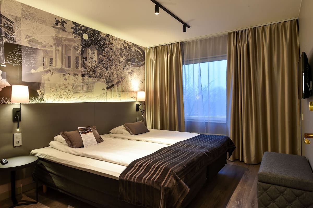 Ein Hotelzimmer mit einem großen Bett, einem Schreibtisch, einer Lampe und einer Wand mit Stadtbild-Fresko.