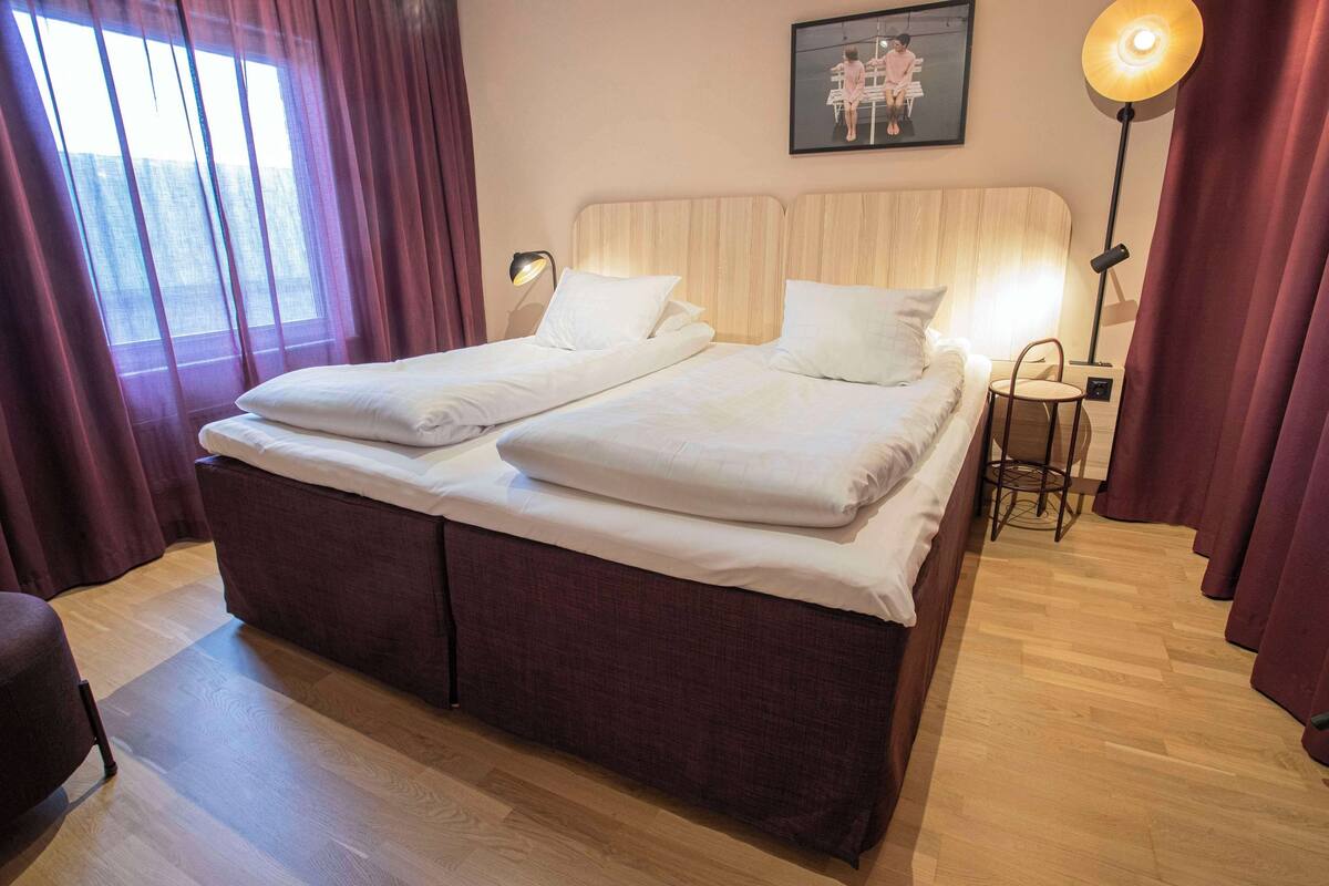 Ein Doppelbett mit Holzfußteil, ein Nachttisch mit Lampe und ein gerahmtes Bild an der Wand.