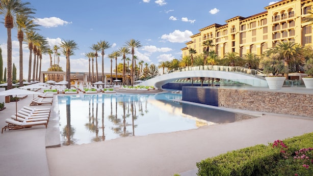 A resort pool with lounge chairs, palm trees, and a stone wall.