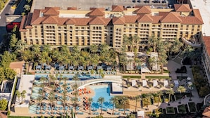 Ein Hotel mit großem Poolbereich, mehreren Etagen und Palmen.