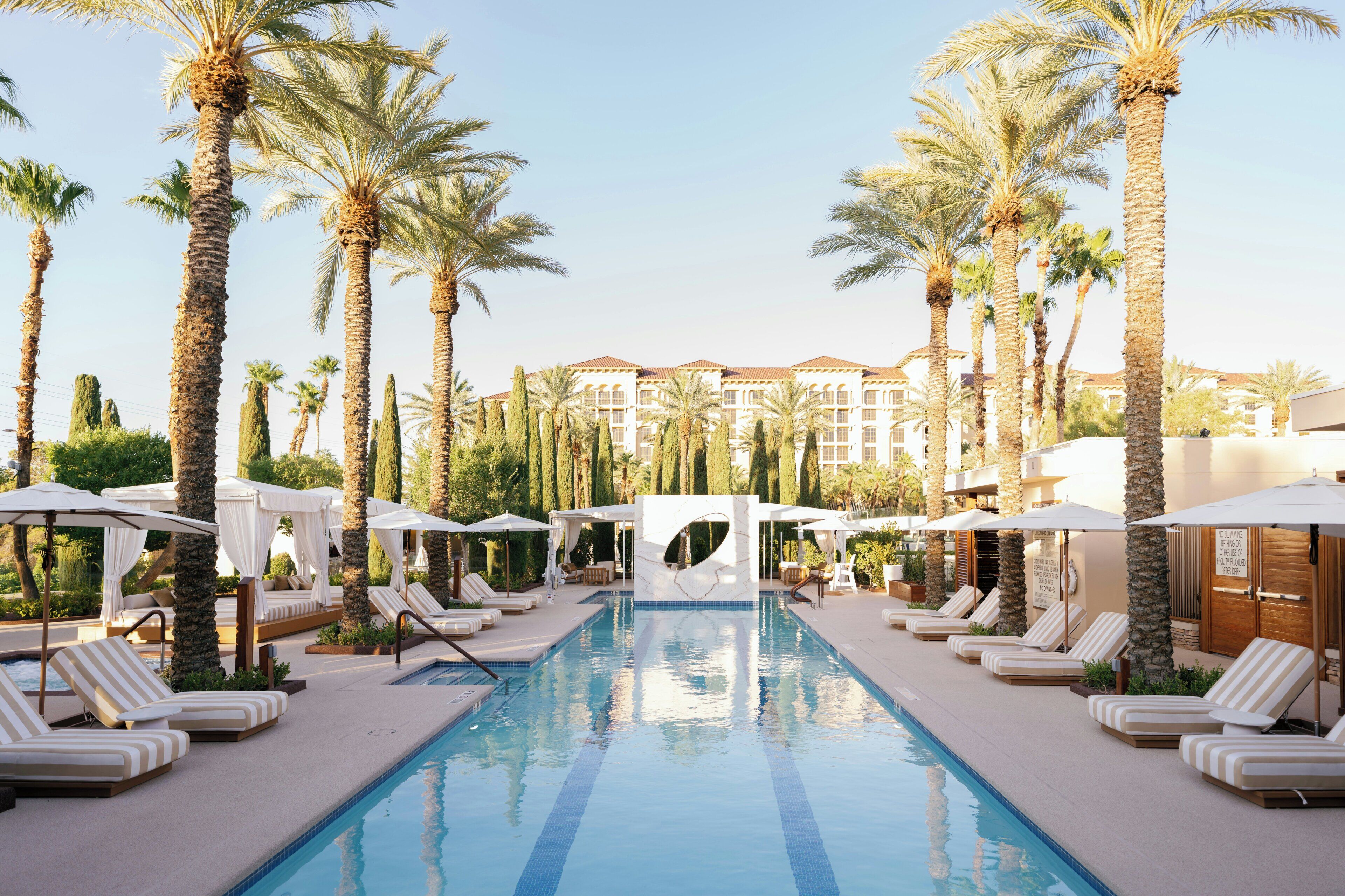 A pool area with lounge chairs, palm trees, and a building in the background.