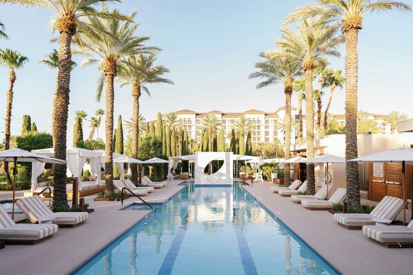 A pool area with lounge chairs, palm trees, and a building in the background.