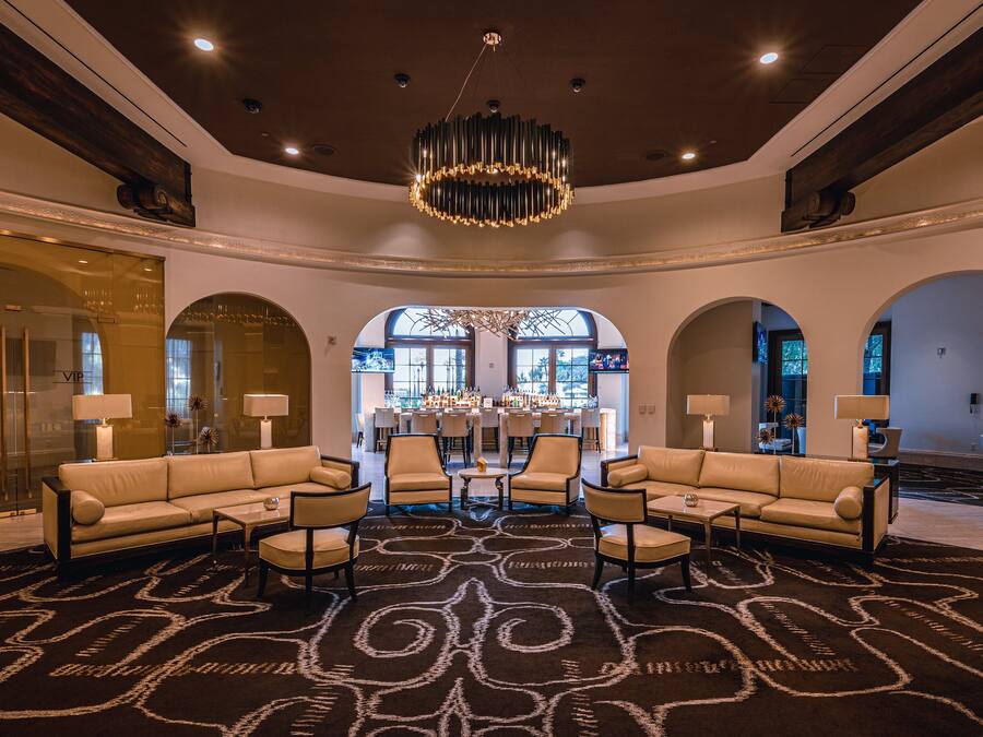 A spacious lobby with a central seating area, a bar in the background, and a large chandelier.