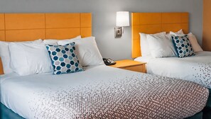 A hotel room with two beds, a nightstand with a phone, and a wall-mounted lamp. - Quiet Corner Inn (Brooklyn)
