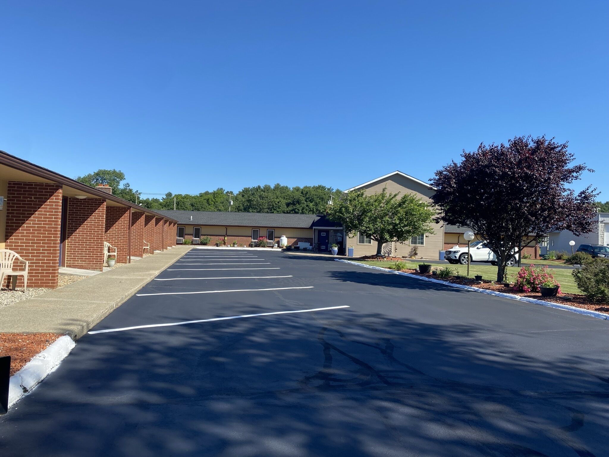 A motel with a parking lot, brick buildings, and a tree.