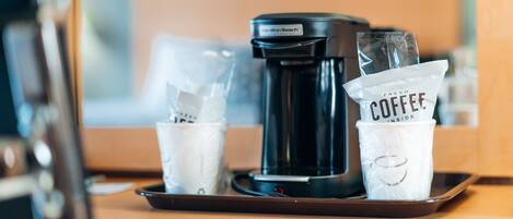 A coffee maker on a tray with two disposable cups labeled "FRESH COFFEE INSIDE" and a plastic bag.
