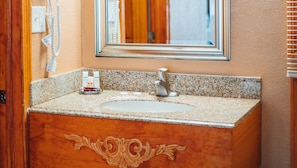 A bathroom with a granite countertop, a sink, and a mirror. There is a towel rack and a soap dispenser on the wall.