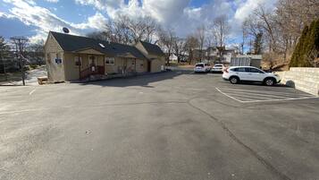 A parking lot with several cars, a building with a satellite dish, and leafless trees.