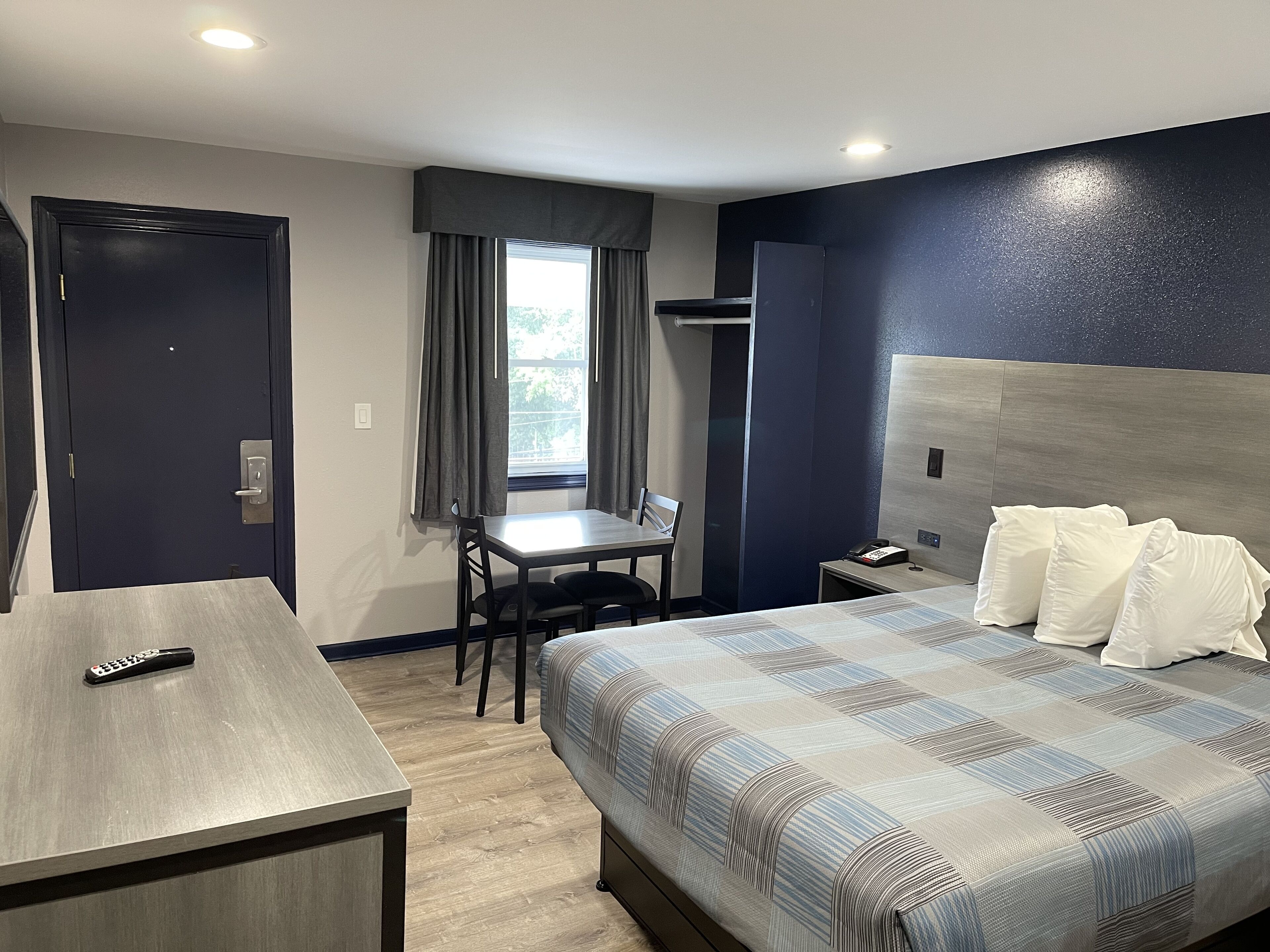 A hotel room with a bed, a desk, a chair, a telephone, and a window with curtains.