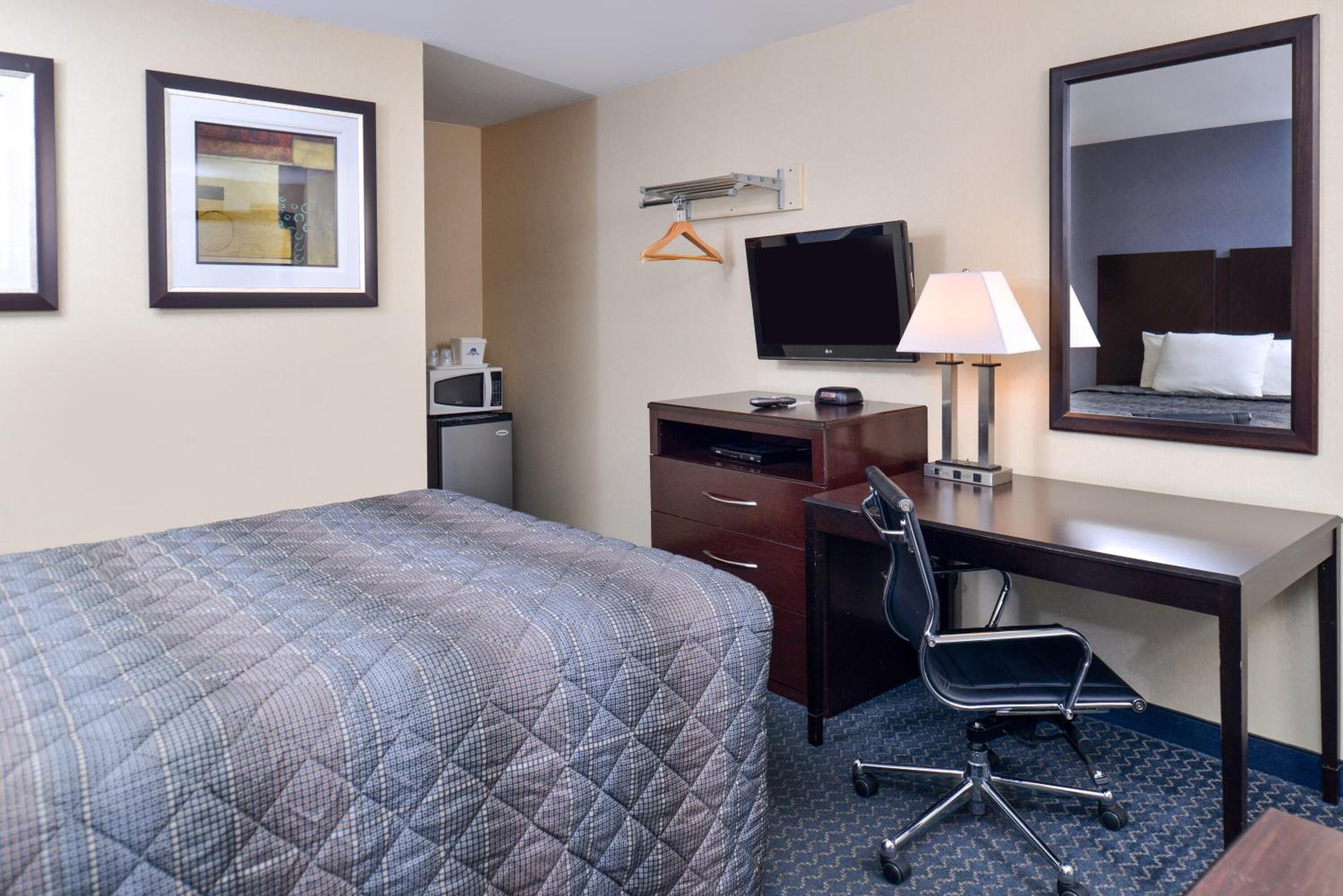 A hotel room with a bed, a desk, a chair, a television, a mirror, and a microwave.