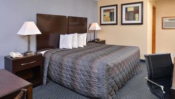 A hotel room with a large bed, two bedside tables with lamps, a desk, and a chair. There are two framed pictures on the wall.