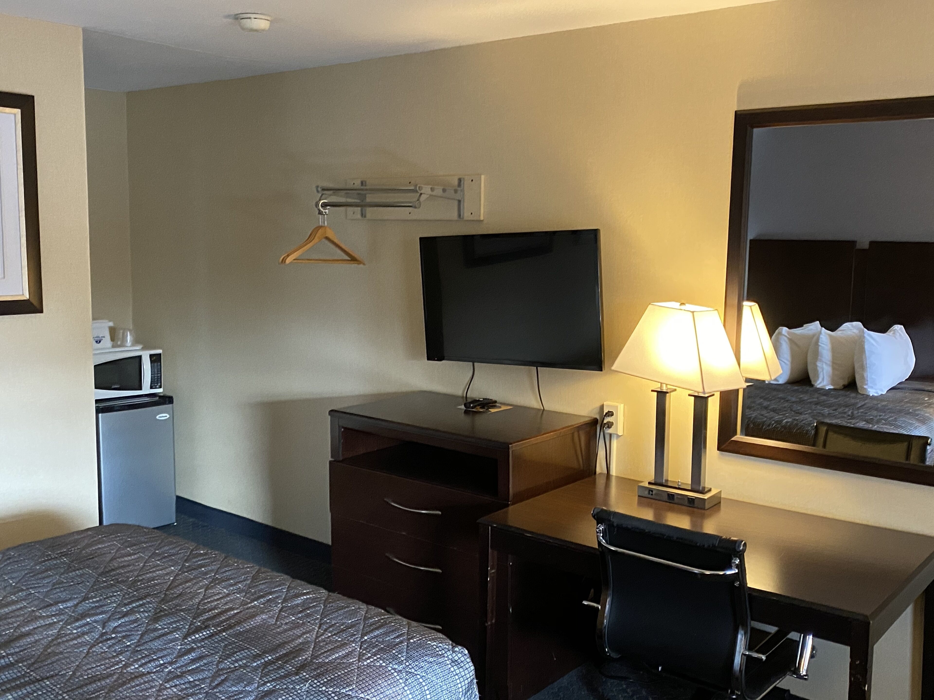 Una habitació d'hotel amb un llit, escriptori amb làmpada, televisió, microones i nevera petita.