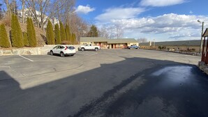 A parking lot with several cars, a building with a green roof, and trees in the background. - Golden Hill Inn Danbury (Danbury)