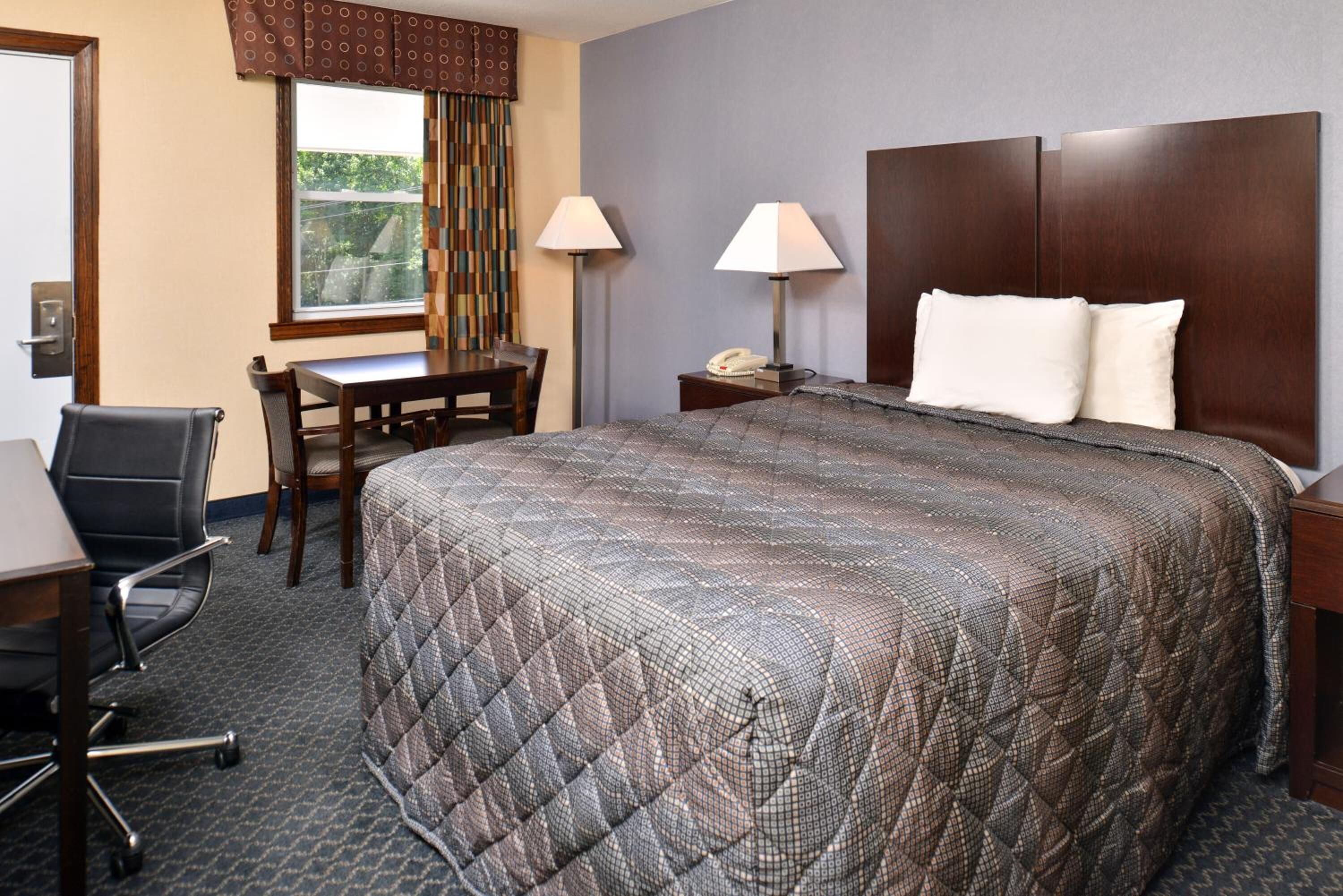 Une chambre d’hôtel avec un grand lit, un bureau, une chaise et une table de chevet avec une lampe.