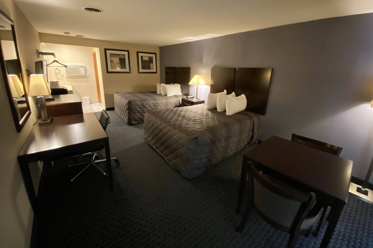 A hotel room with two beds, a desk, a chair, a mirror, and a lamp.