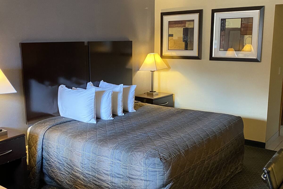 A hotel room with a large bed, a nightstand with a lamp, and two framed pictures on the wall.