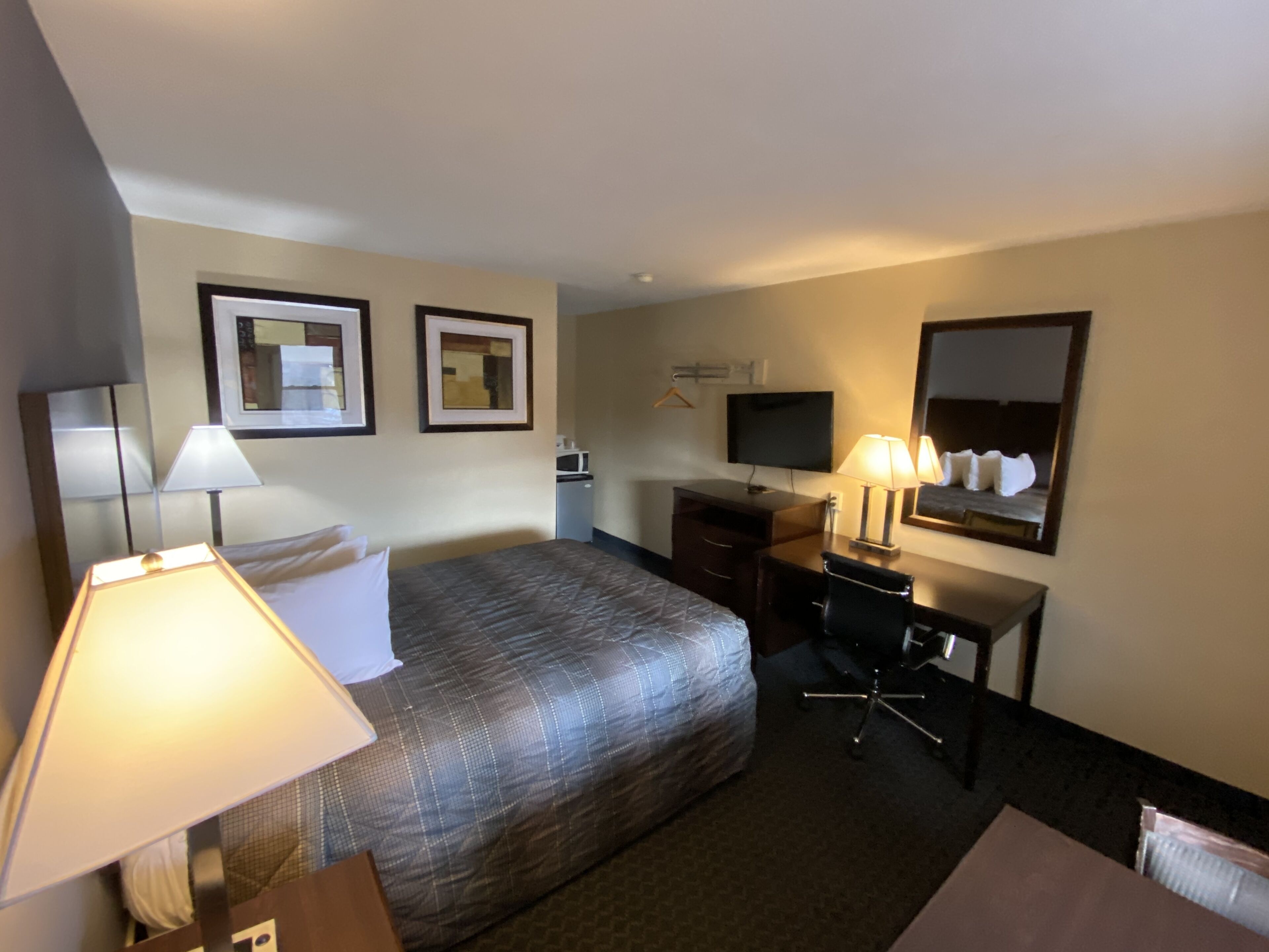 Habitación de hotel con cama, escritorio, silla, lámparas, televisor y espejo.