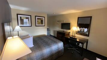 Habitación de hotel con cama, escritorio, silla, lámparas, televisor y espejo.