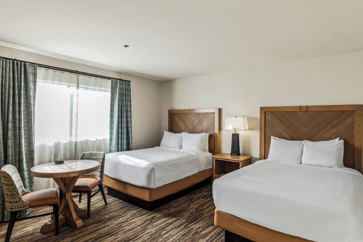 A hotel room with two beds, a round table, and a chair.