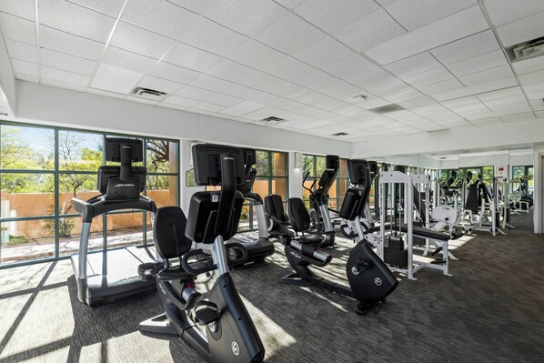 Un gimnasio con máquinas de cardio, pesas libres y un muro de espejos.