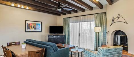A room with a wooden dining table, a sofa, a patterned armchair, a television, and a fireplace.
