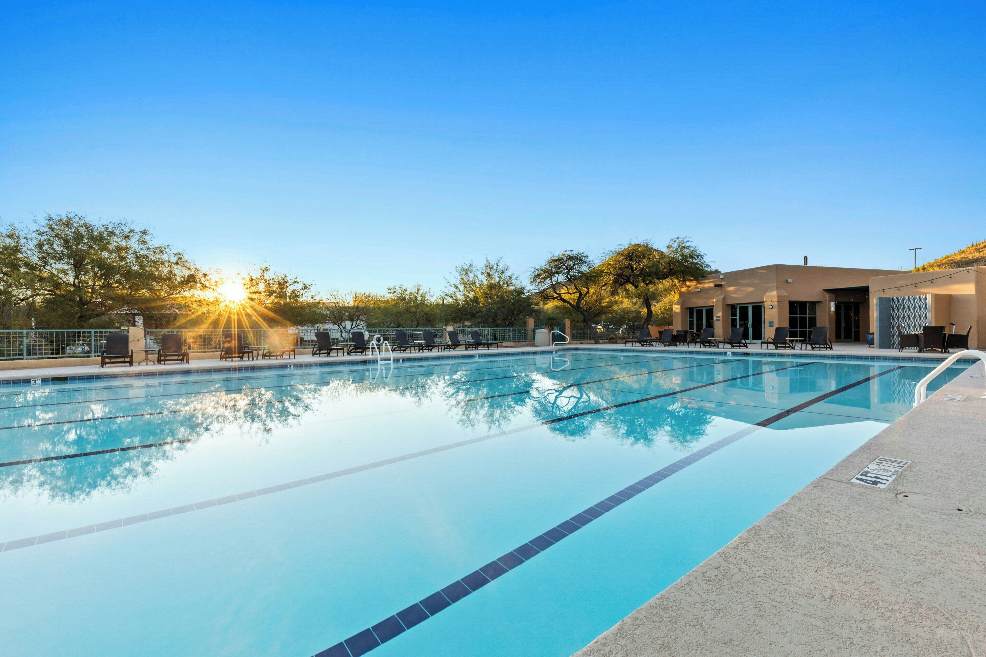A clear swimming pool with lounge chairs and a building in the background.