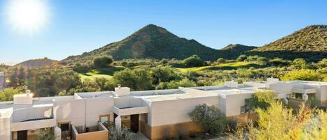 A modern building complex with multiple structures, surrounded by greenery and a mountain in the background.