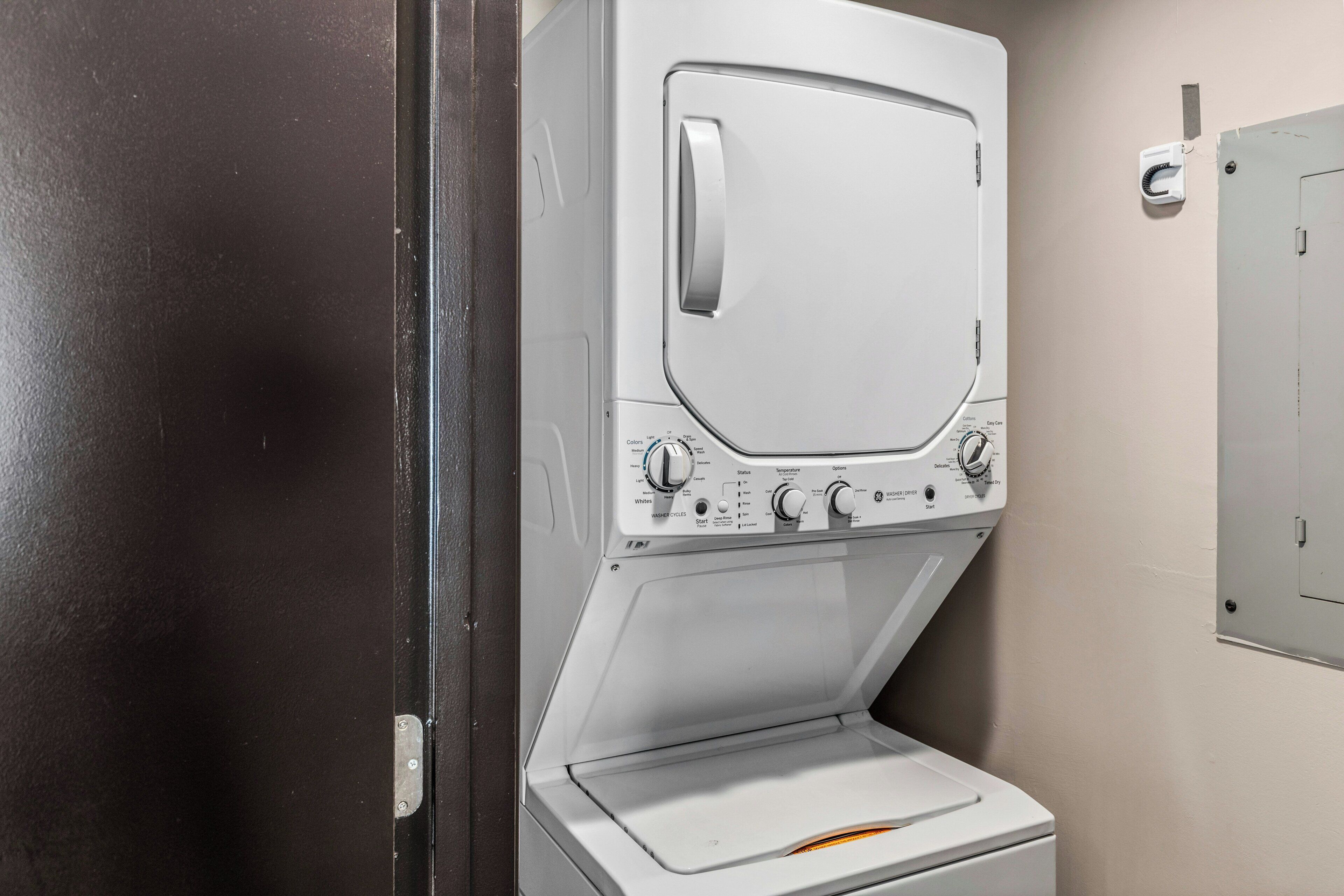 A white front-loading washing machine in a room with a dark door and light walls.