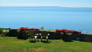 A view of a lake with chairs and a stone wall with red flowers.