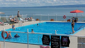A swimming pool with people sunbathing and swimming, surrounded by a white fence.