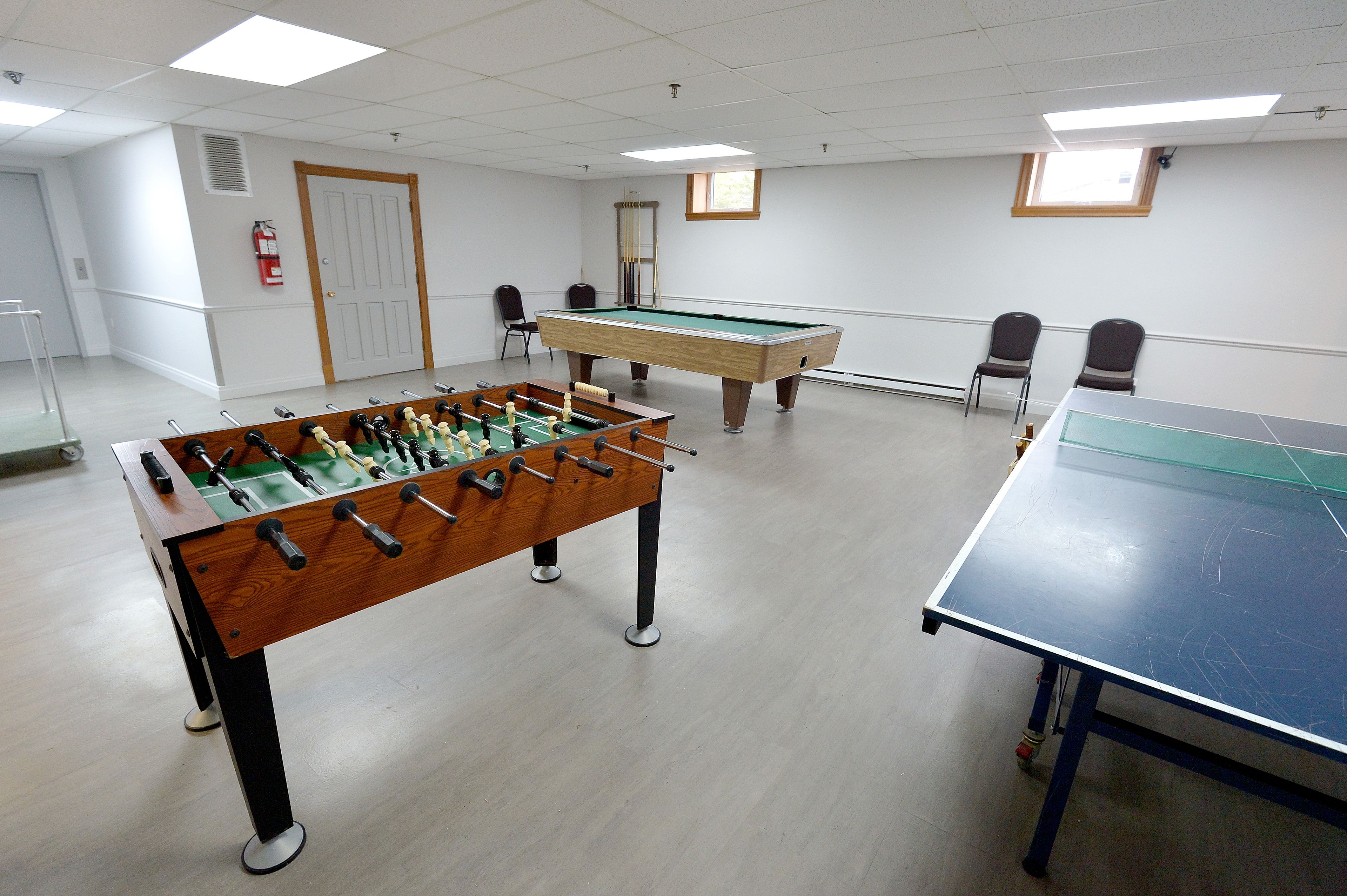 A room with a foosball table, a pool table, and two chairs.