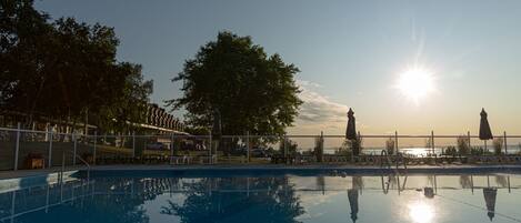 A swimming pool with a clear view of the sunset, surrounded by a fence and trees.