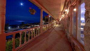 A covered walkway with a view of the sea, potted plants, and a stone wall.