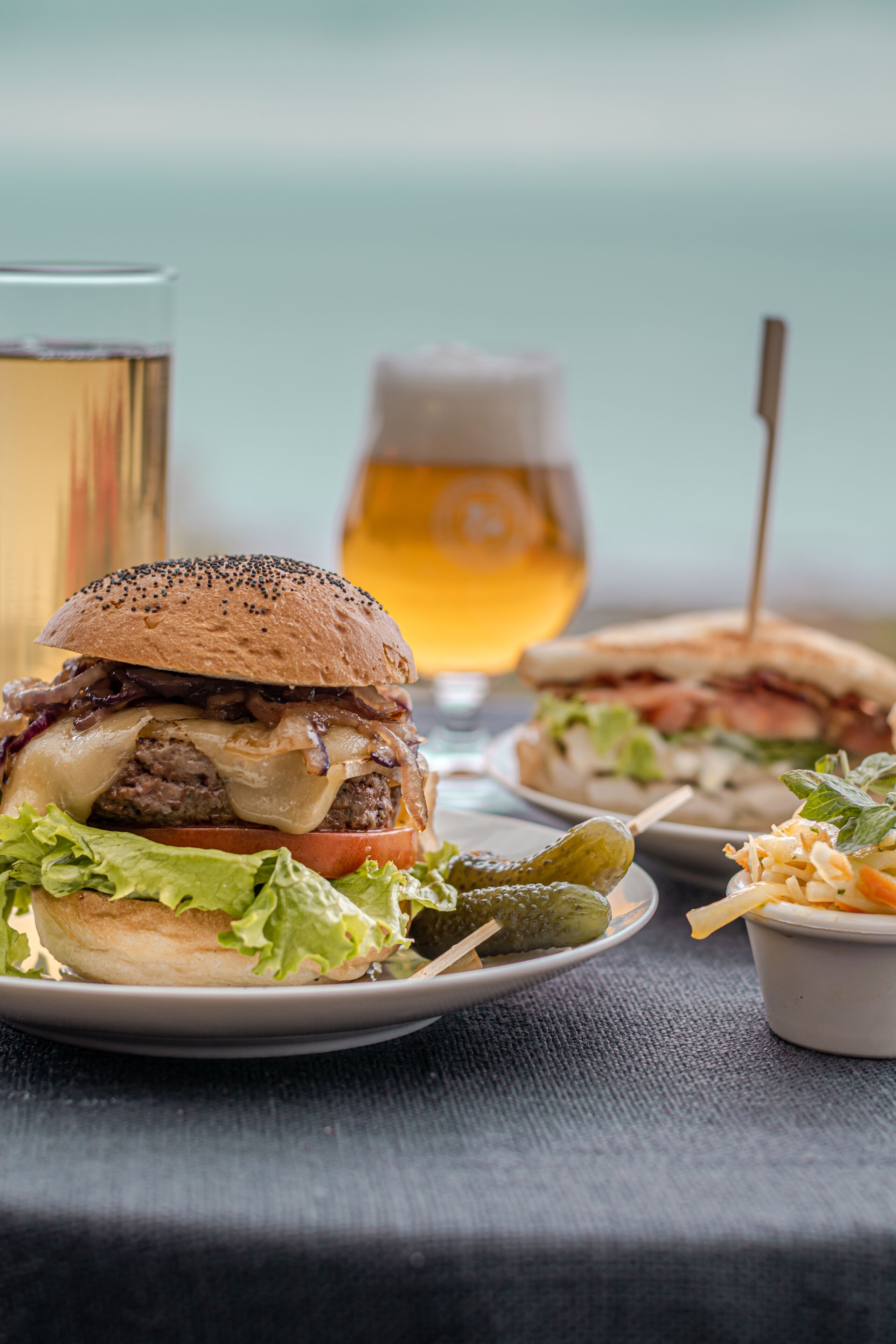 A burger with pickles and a glass of beer on a table.