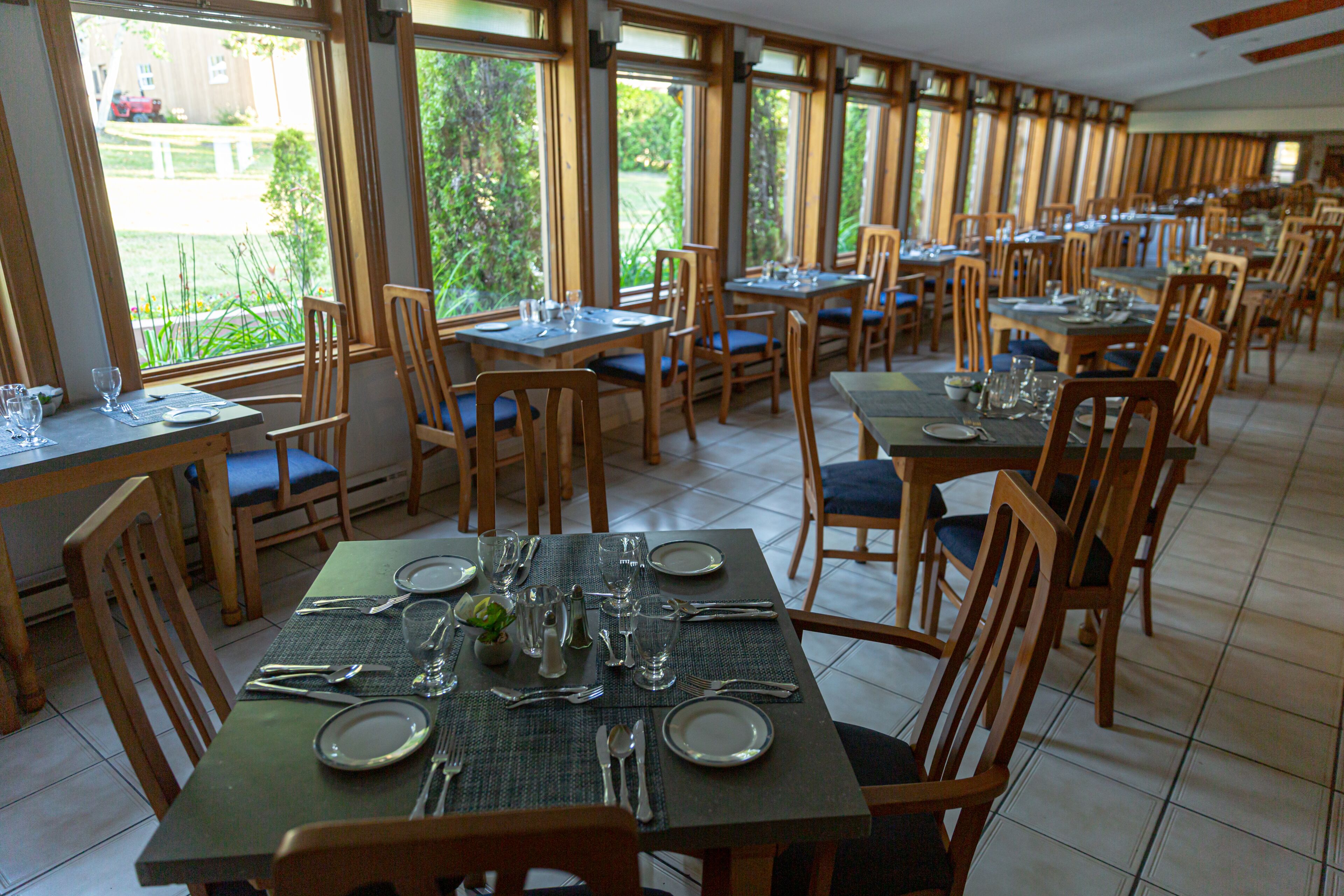 Un restaurante con varias mesas y sillas, dispuesto en un amplio comedor con grandes ventanales que ofrecen vistas al exterior.