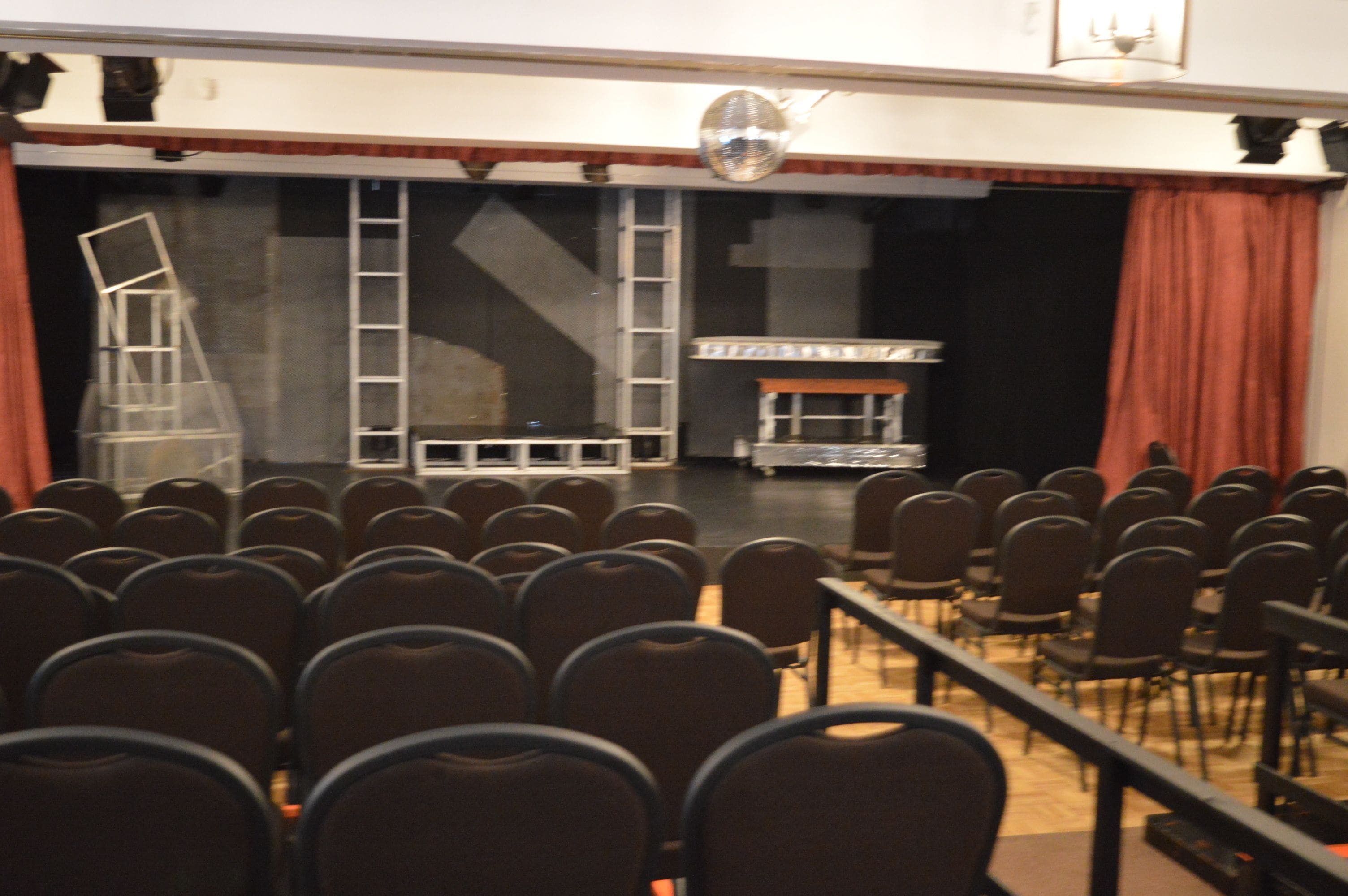 An auditorium with rows of chairs, a stage with a piano, and a disco ball.