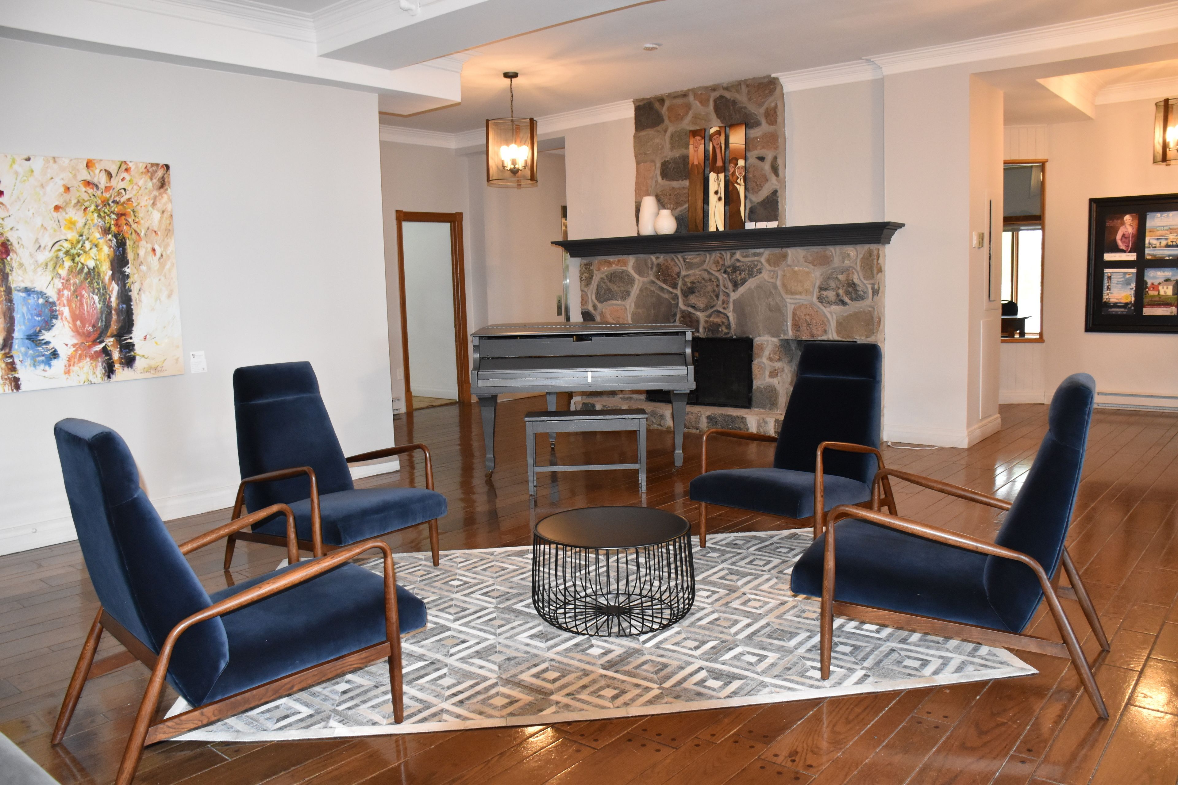 Una sala de estar con chimenea de piedra, un piano de cola y sillones tapizados en azul.