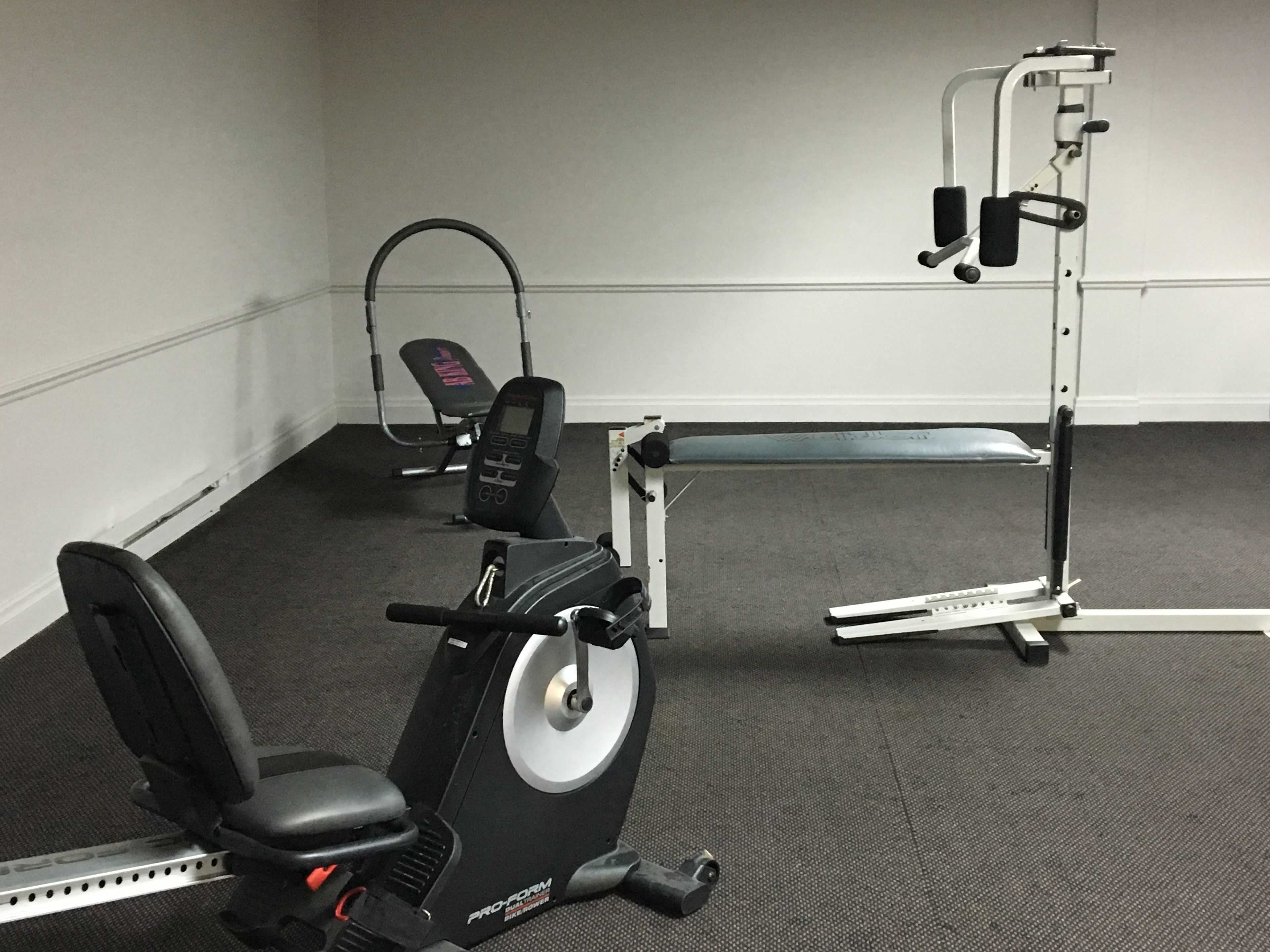 A gym with cardio equipment, a weight bench, and a squat rack.