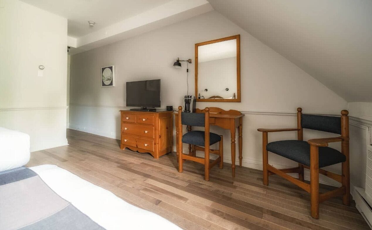 A room with a wooden floor, a desk with a chair, a television, a dresser, and a large mirror.