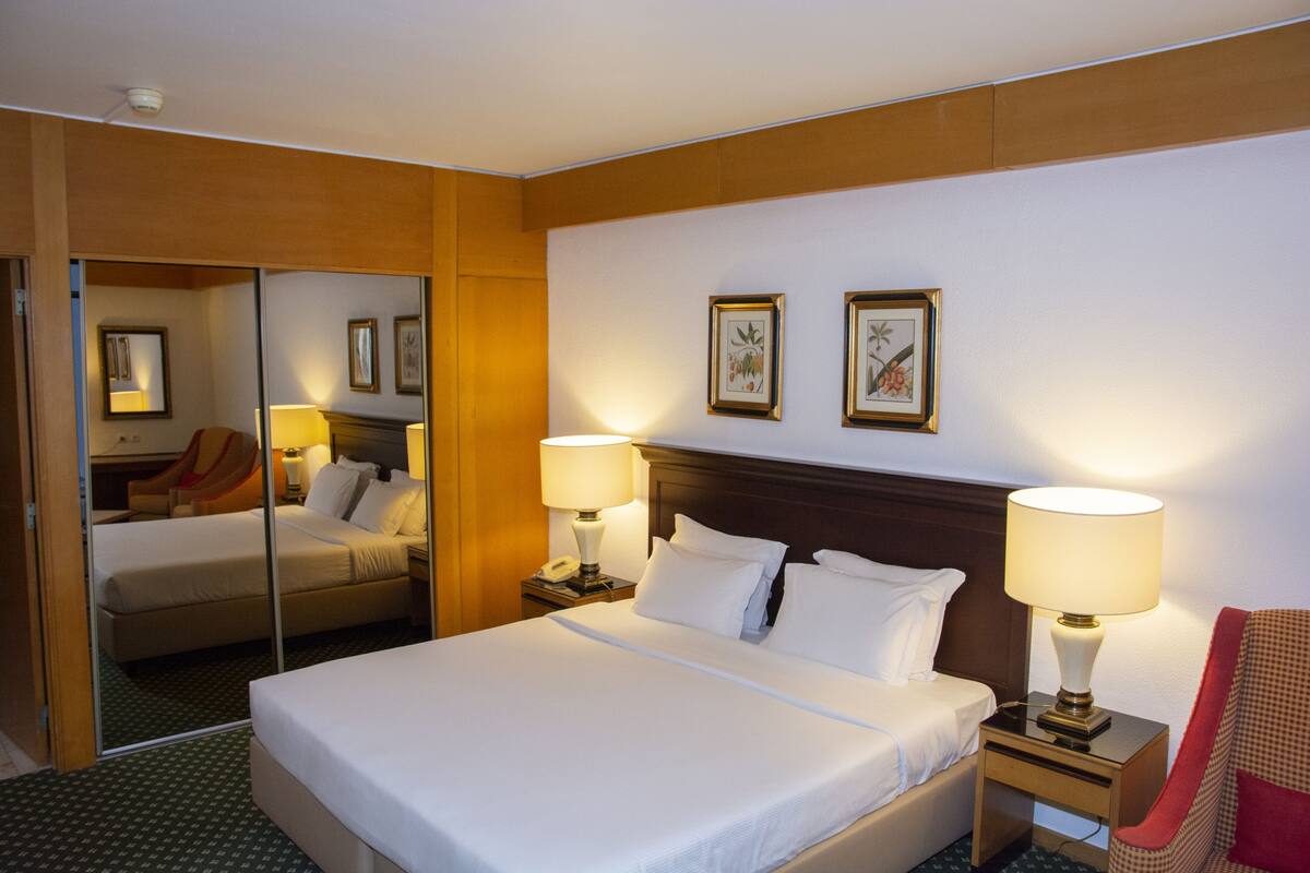 Habitación de hotel con una cama grande, dos lámparas de noche, una mesita de noche, una silla y un espejo.