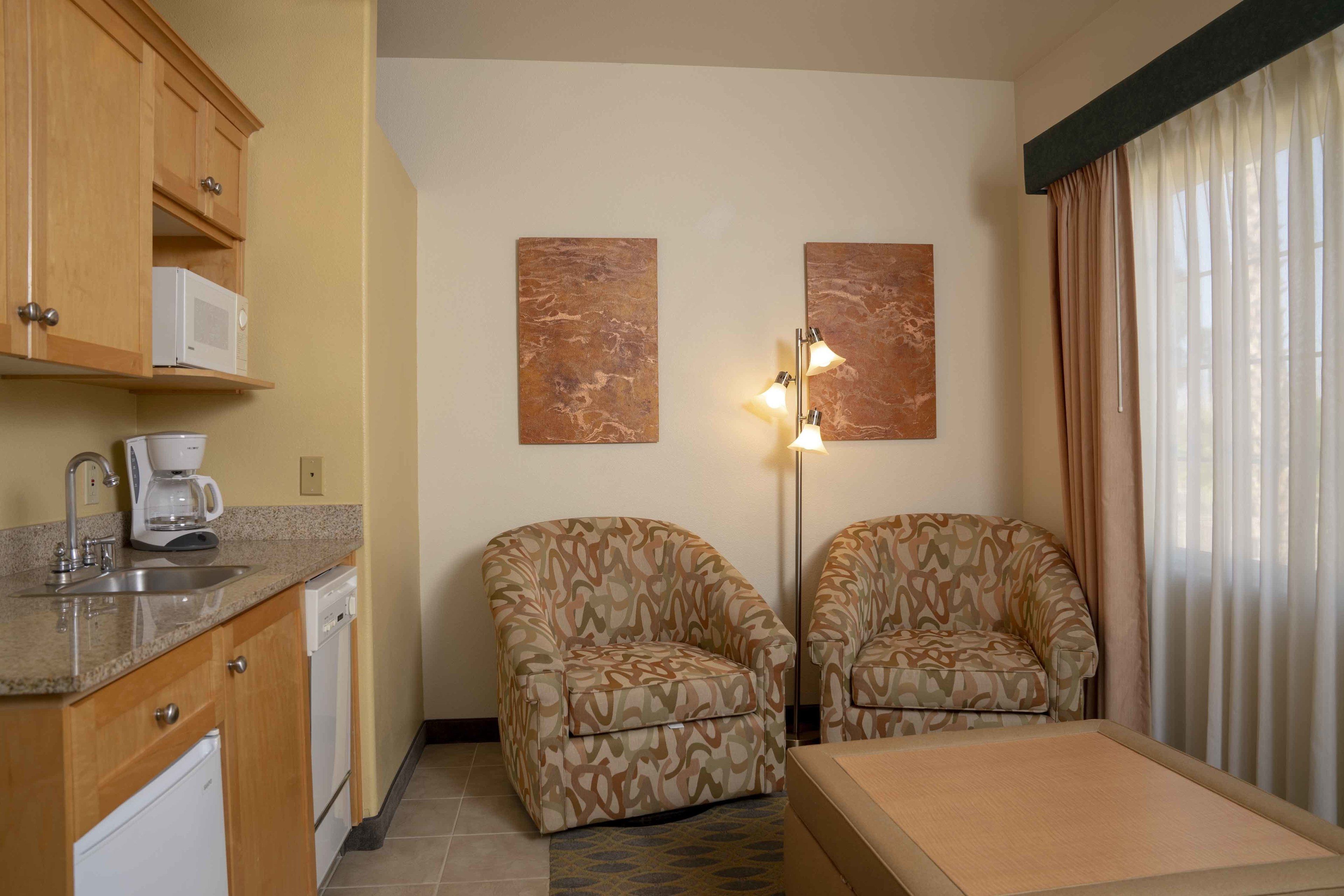Een compacte hotelkamer met een kitchenette, twee gestreepte fauteuils, een klein tafeltje en kunst aan de muren.