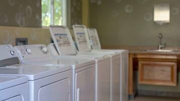 A row of white front-loading washers in a laundry room with a wooden cabinet and a wall-mounted light fixture.