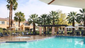 A swimming pool with lounge chairs and umbrellas, surrounded by palm trees and a building with balconies. - Raintree's Cimarron Golf Resort (Cathedral City)