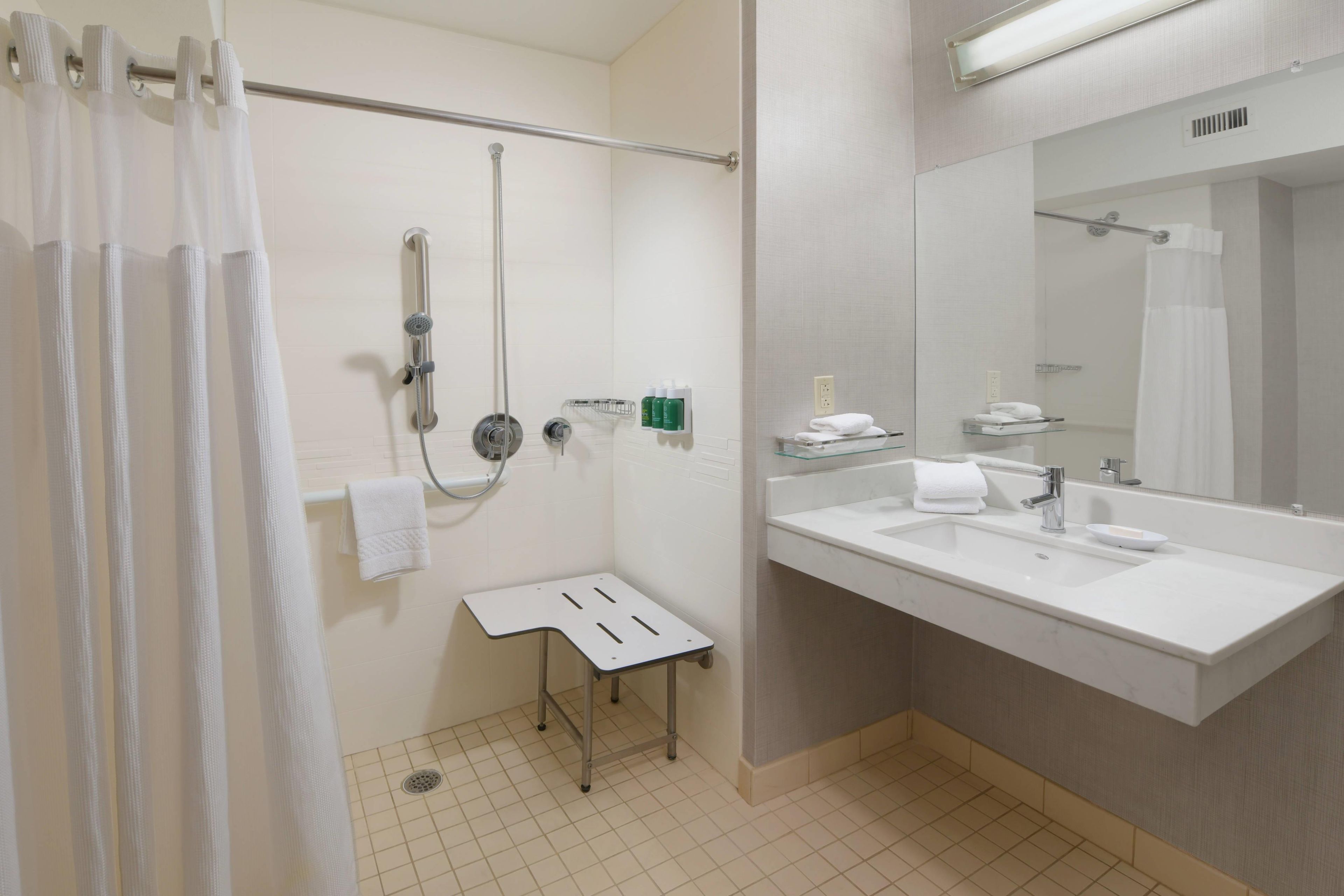 A bathroom with a shower, a sink, a mirror, and a towel rack.