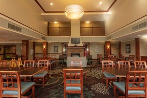 Un hall d’hôtel doté d’une cheminée centrale, de plusieurs tables et chaises, et d’un haut plafond orné d’un grand lustre.